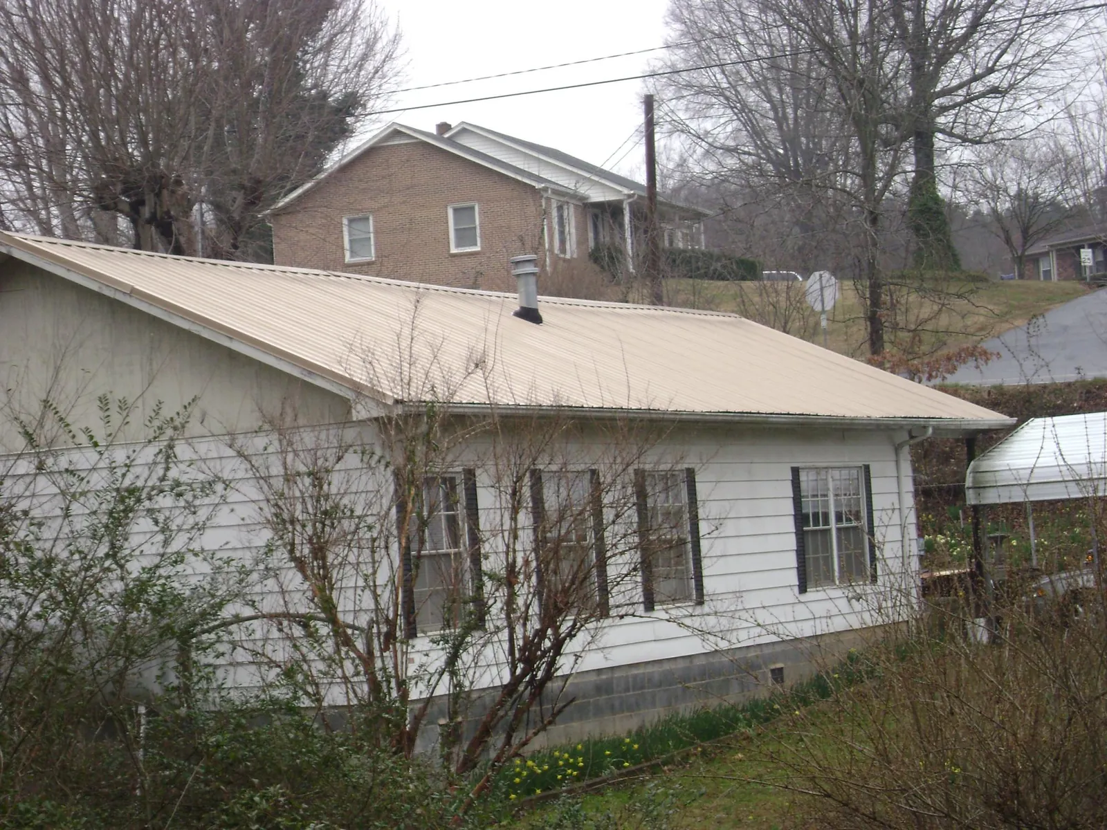 Tan metal roof on a white sided house set into a hillside — Commercial Roofing by Roofing Brothers in Fairfield
